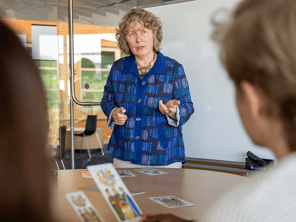 A person in a blue shirt stands in a classroom and appears to be teaching two students in the foreground.