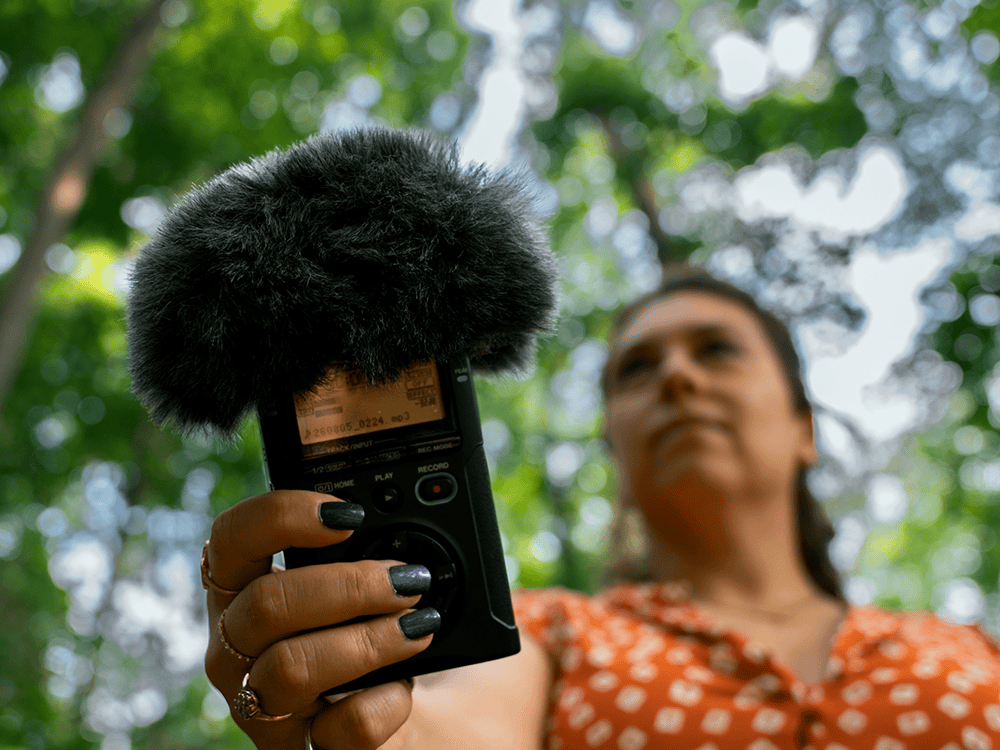 A person in an orange dress holds a piece of audio recording equipment. 