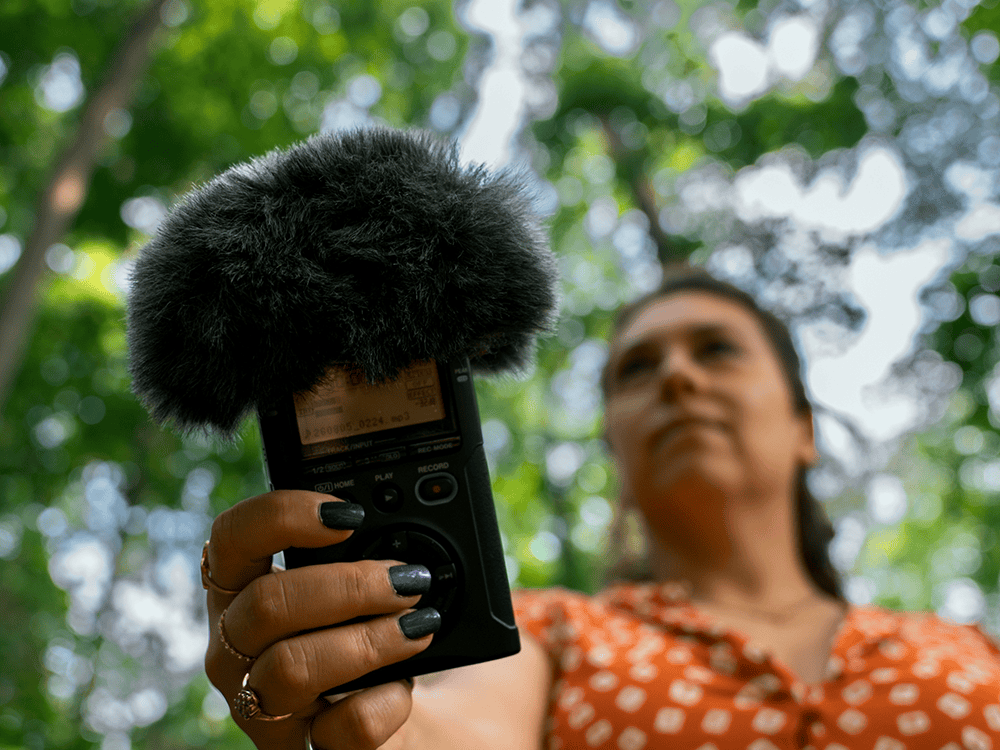 A person in an orange dress holds a piece of audio recording equipment. 