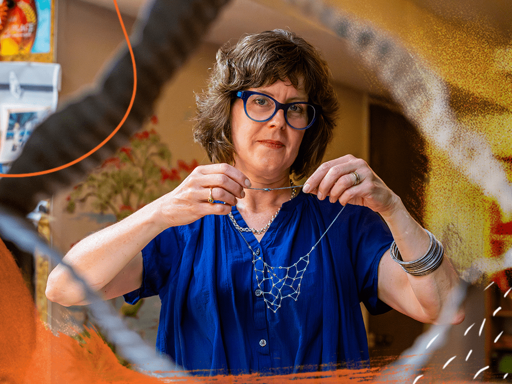 On the other side of a corrugated metal sculpture, a woman holds a silver kinetic necklace.