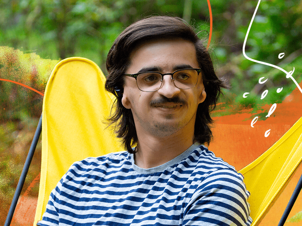 A young man, looking to the right, sits in a bright yellow chair outdoors.