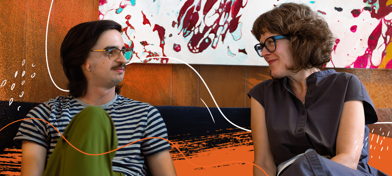 A young man wearing glasses and a striped shirt sits next to a woman wearing a gray dress on a couch.