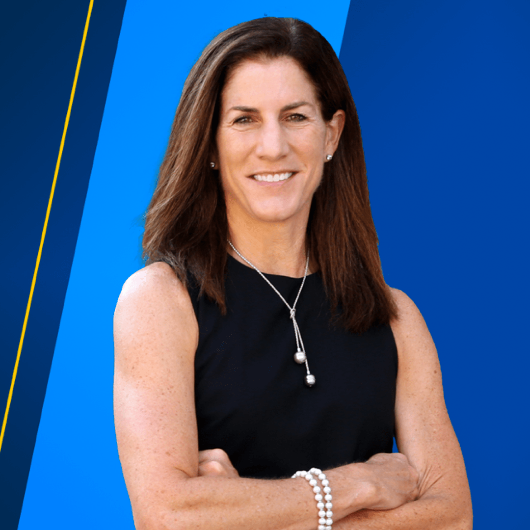 Dean Anne Curzan stands with arms crossed in front of a blue banner.