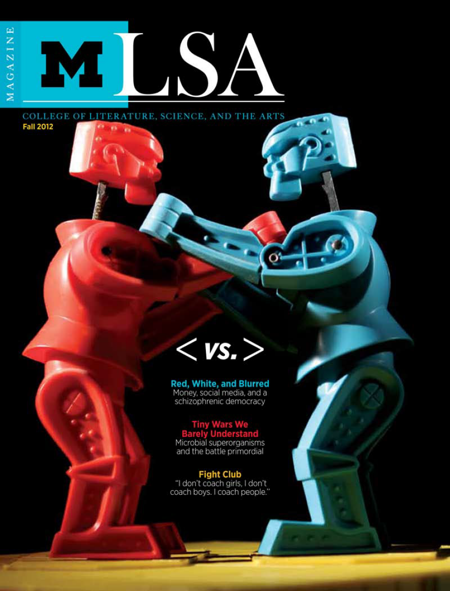 Magazine cover for University of Michigan LSA (College of Literature, Science, and the Arts) Fall 2012 issue. The main image is a close-up of two classic Rock 'Em Sock 'Em Robots toys, one red and one blue, posed as if they are about to battle each other against a black background. The headline reads "< VS. >" between the two robots. Featured article titles in various colors appear below, including "Red, White, and Blurred," "Tiny Wars We Barely Understand," and "Fight Club." The LSA Magazine title is at the top with the University of Michigan block "M" logo.