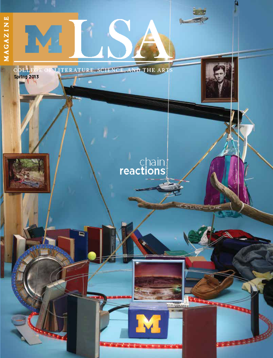 Magazine cover for the University of Michigan LSA (College of Literature, Science, and the Arts) Spring 2013 issue. The cover features an elaborate Rube Goldberg-style setup on a blue background, with a variety of objects linked together, including books, picture frames, a purple backpack, a model helicopter, a toy airplane, a globe, a moccasin, a metal tray, and a blue cube with a yellow University of Michigan "M." The words "chain reactions" appear in white lowercase letters near the center. The LSA Magazine title is displayed at the top over an orange block with the block "M" logo.