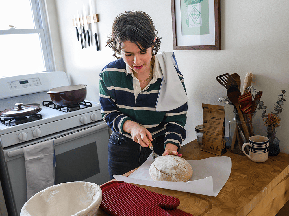 A photograph of a person in their kitchen cutting into a loaf of sourdough bread.