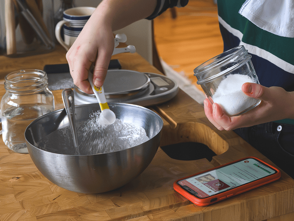 A close-up photograph of a person measuring ingredients into a stainless steel bowl.
