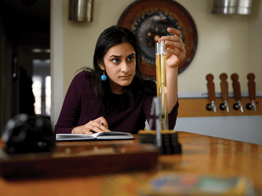 A photograph of a woman examining the contents of a test tube while making notes.
