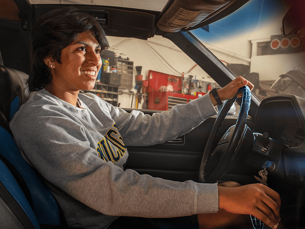 A smiling person sits in the front seat of a Datsun in this image taken from the perspective of the front passenger seat.