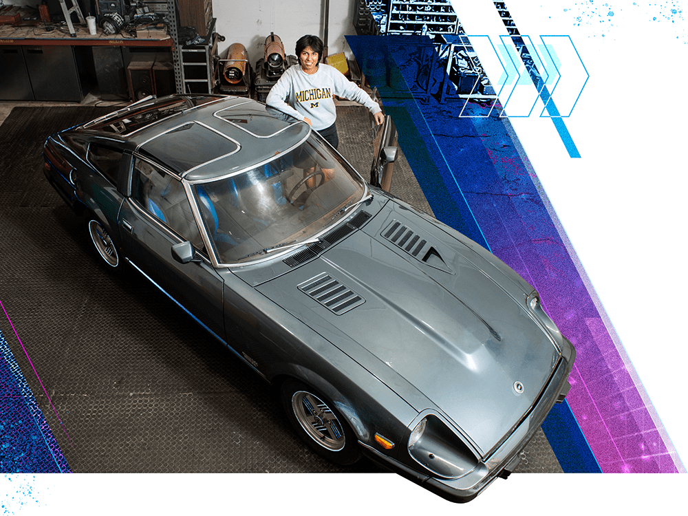 A photograph of a student standing next to the open driver’s-side door of her car from an elevated view.