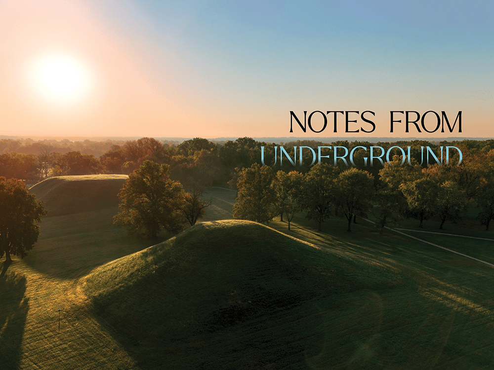 A drone photograph of two earthen mounds, shot at dawn. Text says "Notes from Underground."