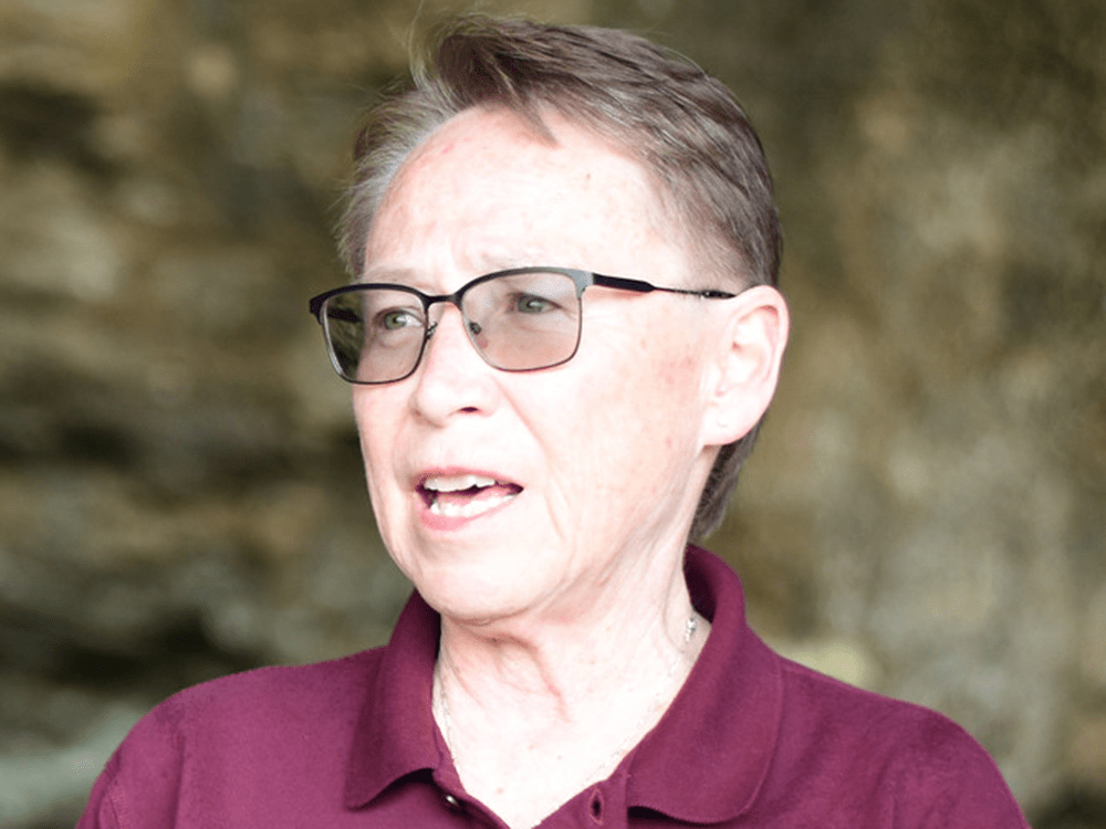 A photograph of a woman wearing a maroon polo shirt in front of a geological feature.