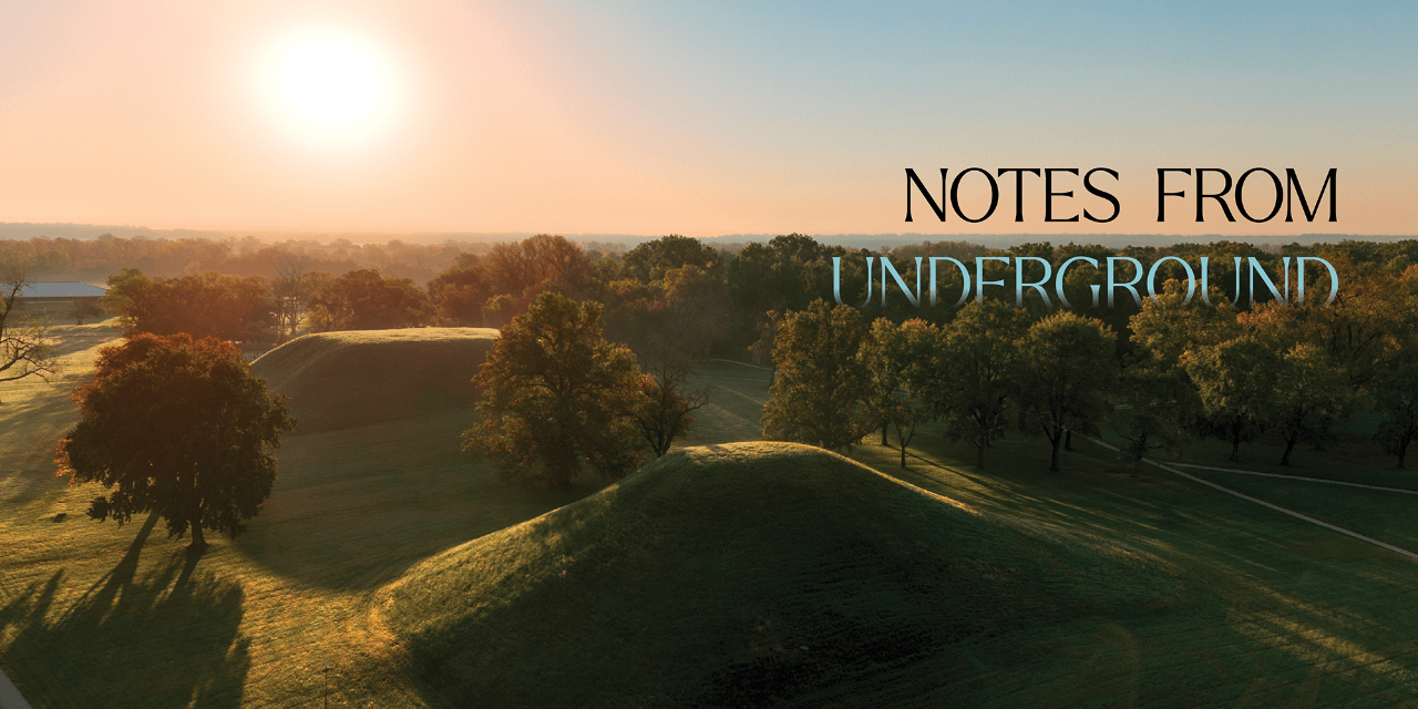 A drone photograph of two earthen mounds, shot at dawn. Text says, "Notes from Underground."