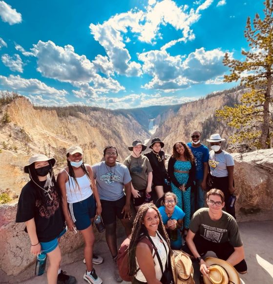A group of eleven young people pose in front of mountains at Yellowstone National Park.