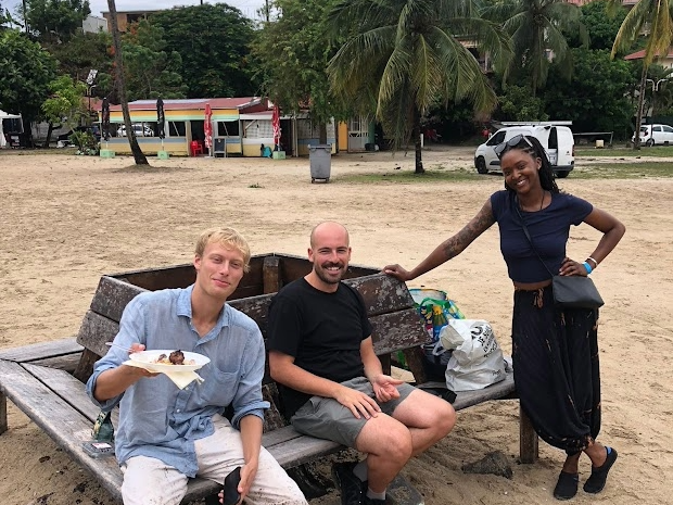Three people gather around a bench on a beach in Martinique