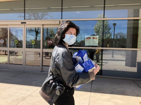 A young woman wearing a protective face mask poses outside a hospital with boxes of face masks, some of the PPE donations from LRCCS friends in China.
