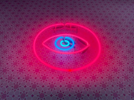 A red and blue neon eye mounted on wallpaper with a repeating star pattern.