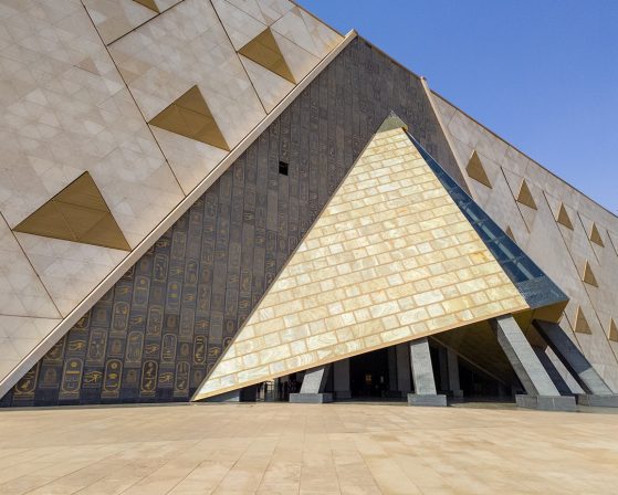 The front entrance of the Grand Egyptian Museum, featuring a triangular, pyramid-inspired entryway surrounded by a wall of hieroglyphs.