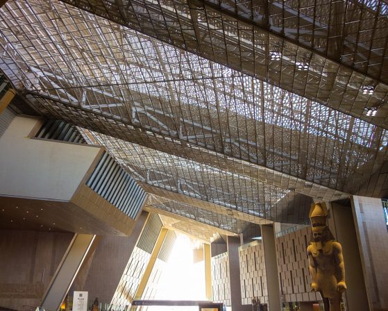 View of the Grand Egyptian Museum’s interior, including its high ceiling with natural light coming through and a monolithic statue of a pharaoh.