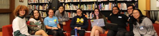 An image of a diverse group of students sitting on a red couch, smiling and facing the camera, in the Language Resource Center lounge area