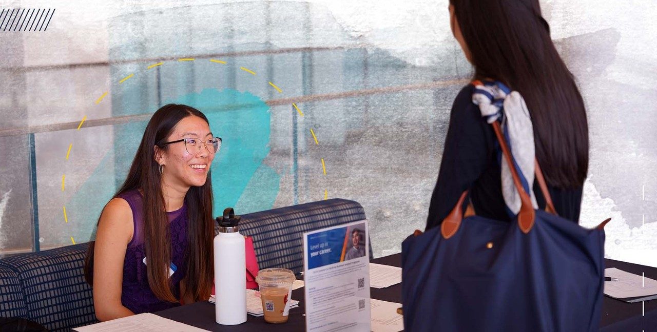 Employer talks to student, while smiling, and sitting at a table