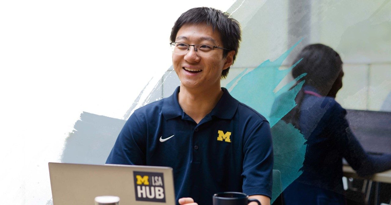 Student working on laptop and smiling at something off camera