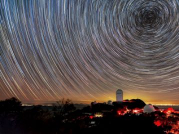 The Dark Energy Spectroscopic Instrument mounted on the U.S. National Science Foundation’s Nicholas U. Mayall 4-meter Telescope at Kitt Peak National Observatory at night with the swirling universe above