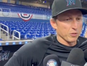 a man with a Marlin's baseball cap in a black t-shirt being interviewed by reporters.