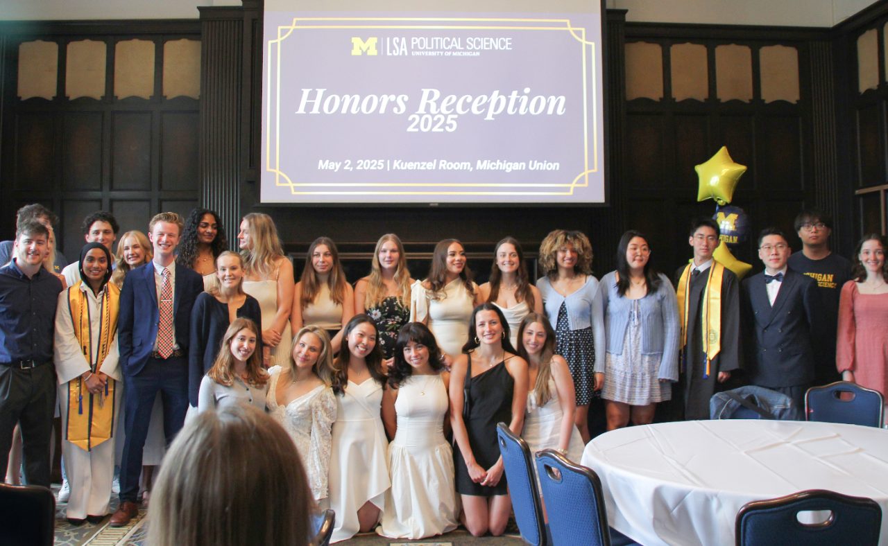21 students in business casual dress gather in front of a projector which reads Honors Reception 2024 May 2, 2024 Kuenzel Room, Michigan Union