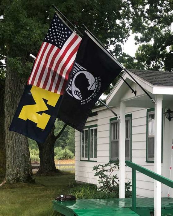 A U-M flag, a U.S. flag, and a POW/MIA flag hang from Sydow's home