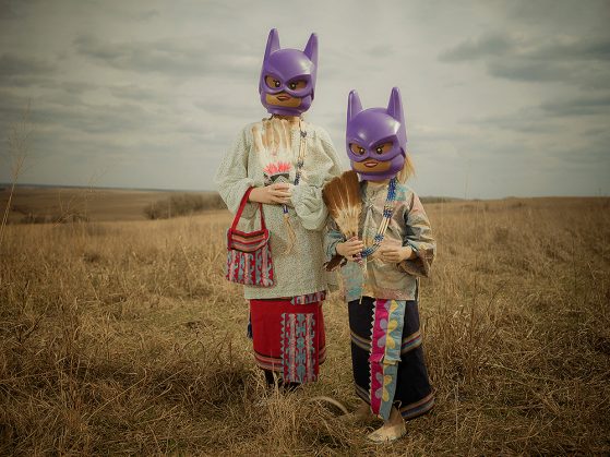 Children dressed in tribal regalia rupture an otherwise traditional pastoral scene by wearing Lego Batgirl masks. Photo by Ryan RedCorn