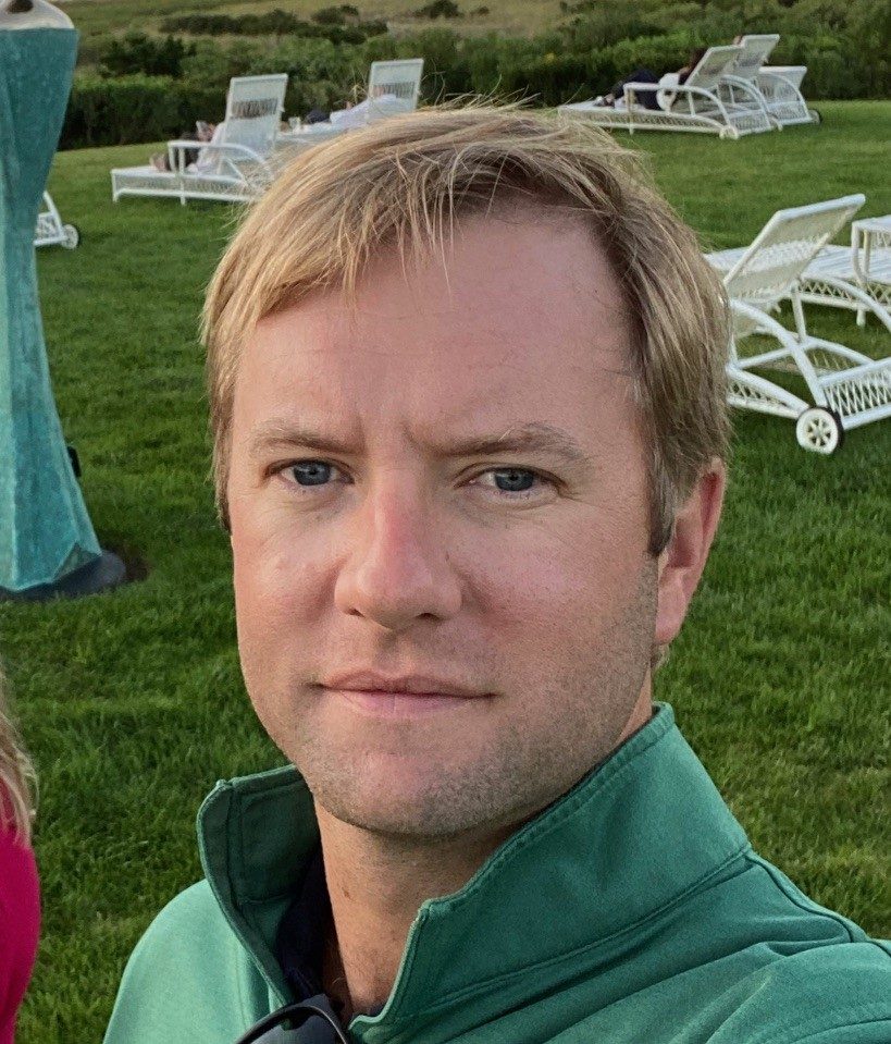 Profile photo of Mark Stephenson wearing a green zipped jacket. Green grass with lounge chairs pictured in the background.
