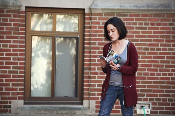 A female student reads from a magazine against a brick wall backdrop