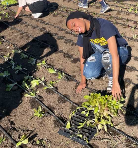female in blue shirt gardening and smiling at camera