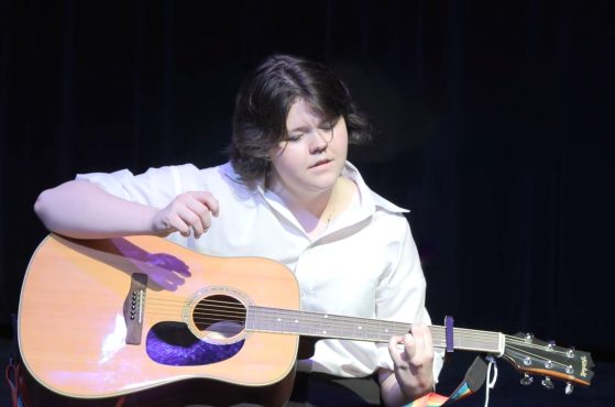 female in white shirt playing guitar on stage