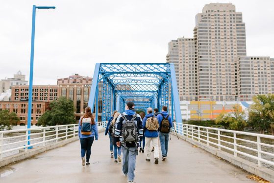 students walk across a blue bridge with large buildings in the background