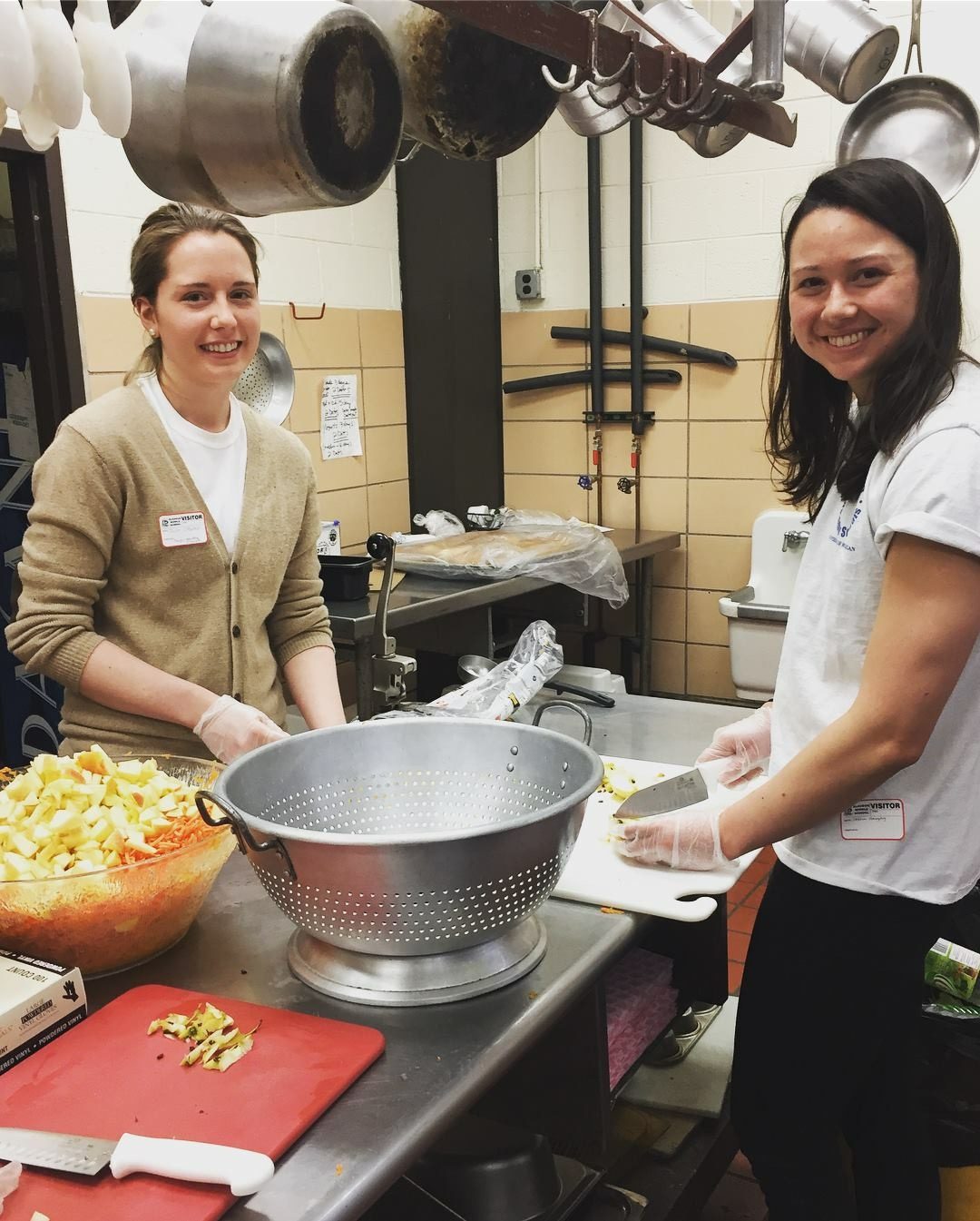 Two female project community students smiling while prepping food in a school kitchen