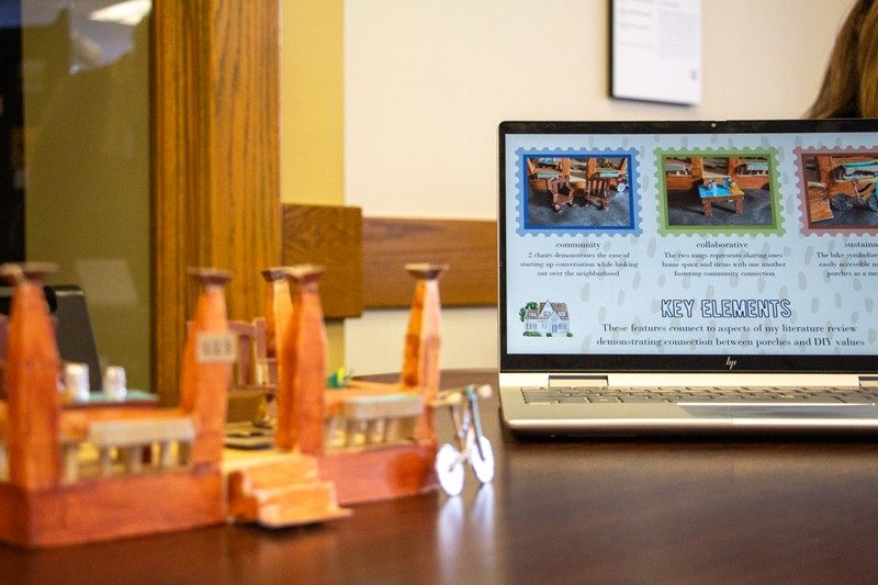 Miniature model of a house porch with laptop in background showing project about porches