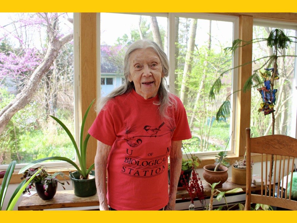 Woman standing in a sunroom surrounded by plants