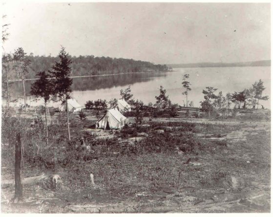 Black and white photo of tents along a lake