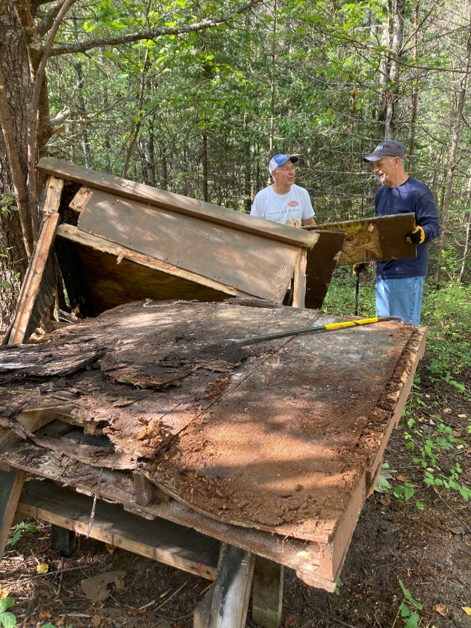Two men tearing apart an old wooden structure in a forest