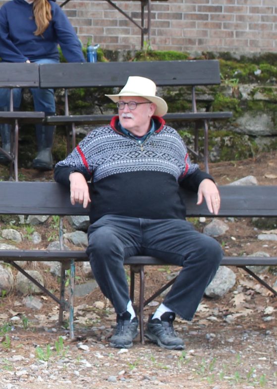 Dr. Nadelhoffer wearing a cowboy hat and nordic patterned sweater, sitting thoughtfully on a bench.