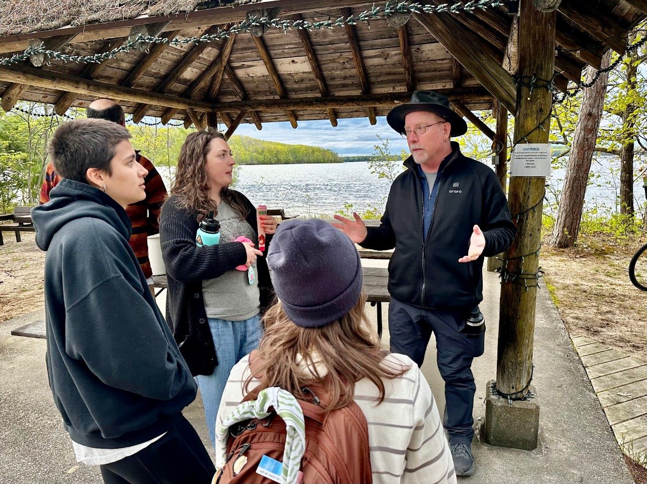 A group of people standing and talking along a lake shore