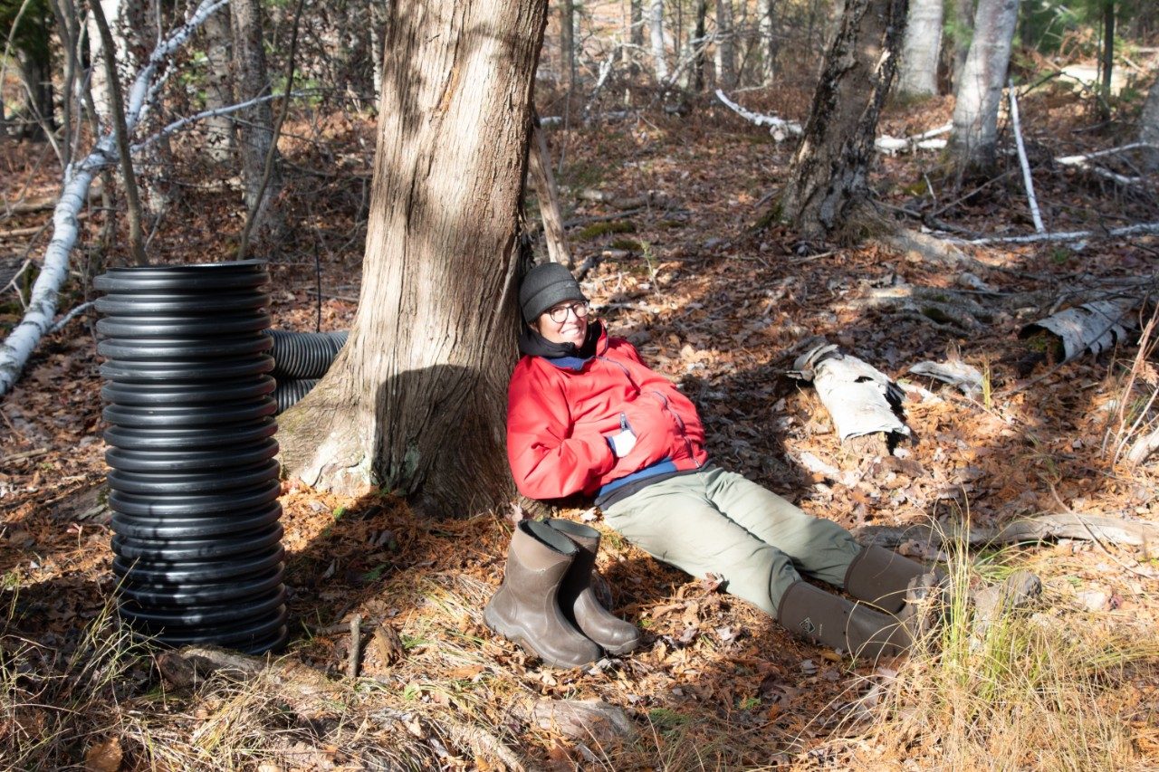 Woman in a forest sitting on the ground and leaning against a tree