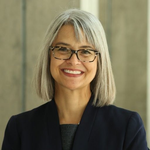 Professor Cole smiles in a black shirt and jacket against a neutral background