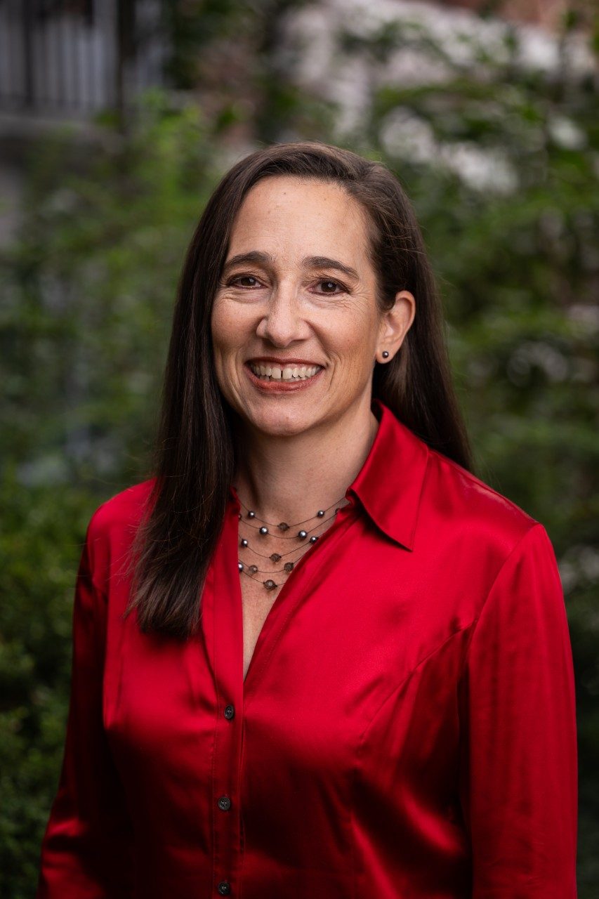 Professor Cortina smiles in a red shirt against a green nature background