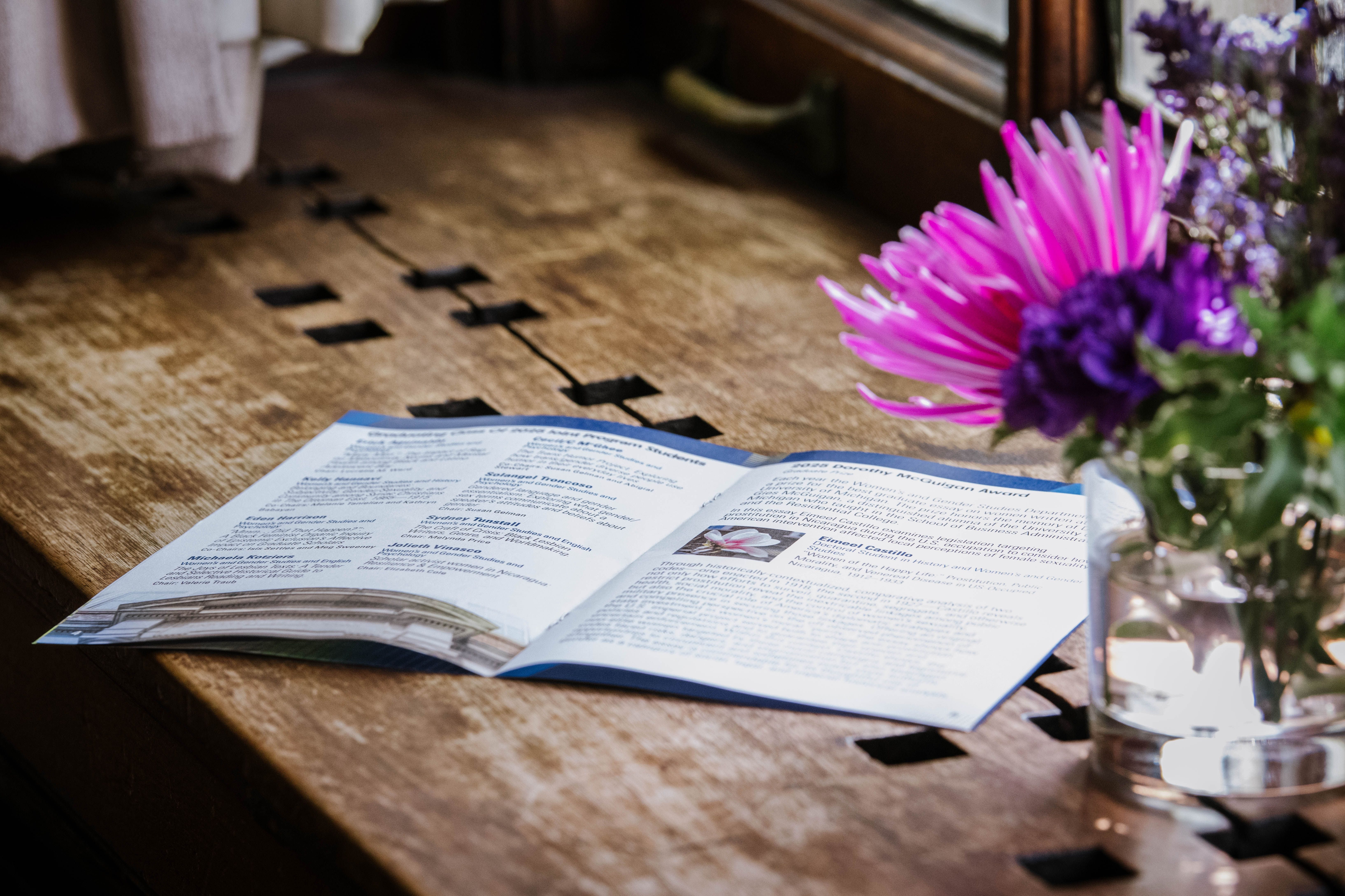 Program on a windowsill next to a vase of flowers