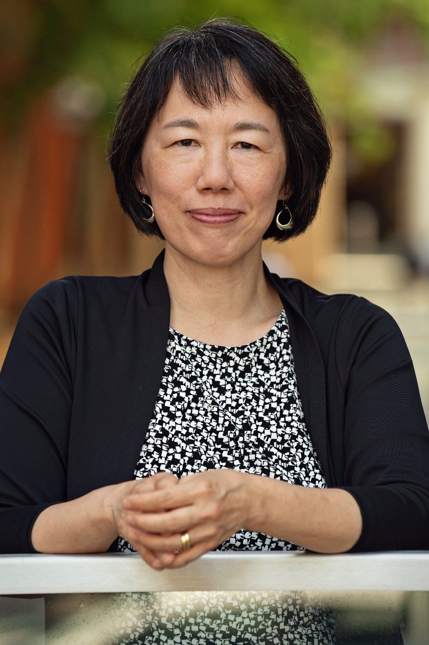 Professor Wu smiles in a black and white shirt against a natural background