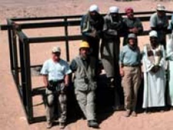 Group photo of the Abydos Middle Cemetery research team on site, standing in front of a black metal frame.