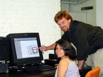 A man and a women pause to smile at the camera while using a GIS computer.